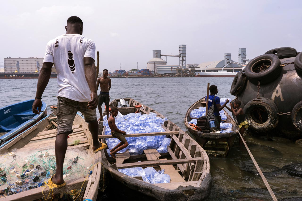 Young men and boys standing and sitting on wooden boats filled with water sachets