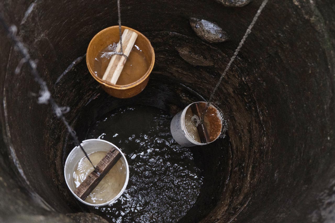 Three buckets full of water being pulled up out of a well by rope