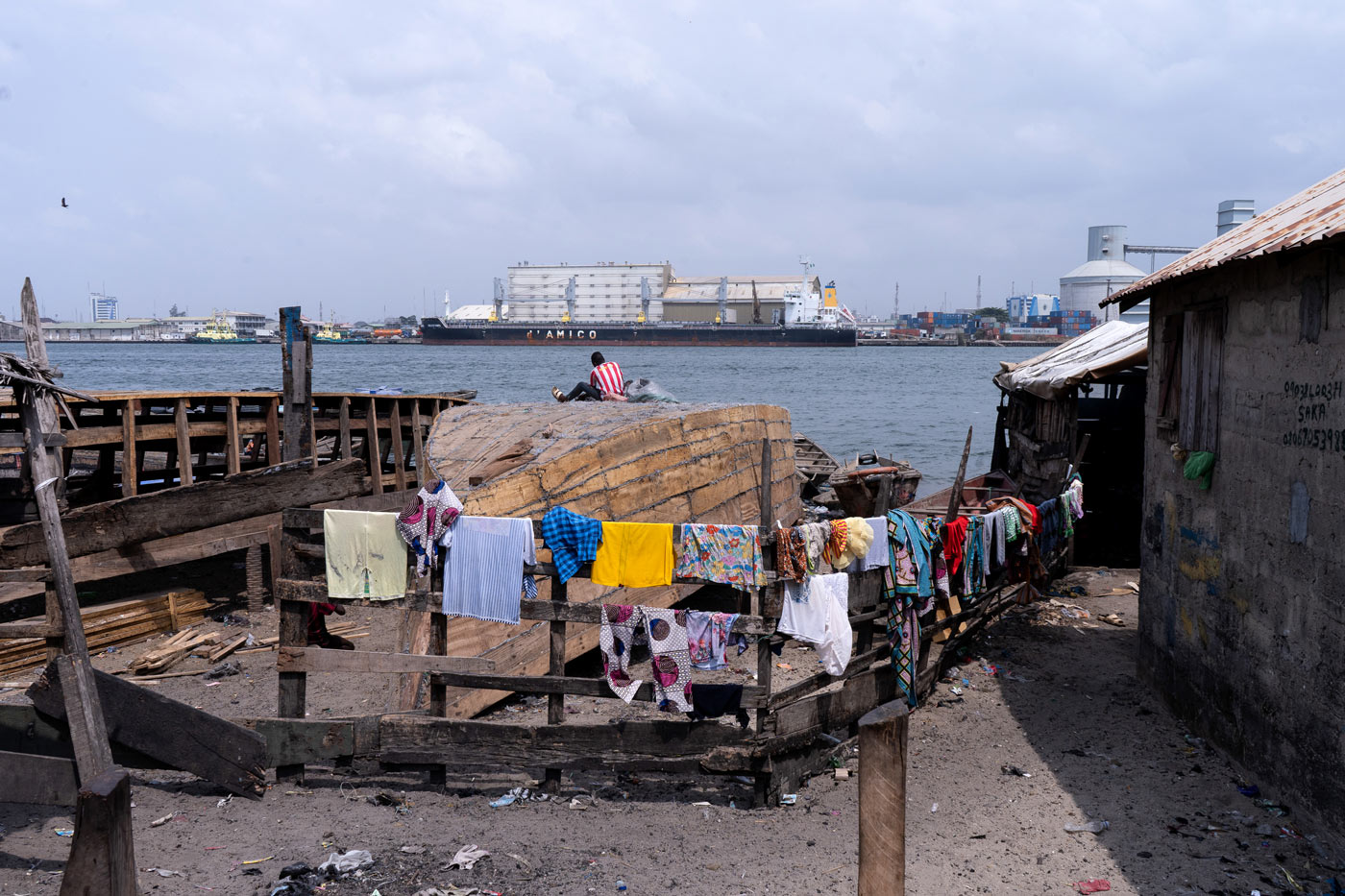 A young man working on top of an overturned wooden boat that is under construction on the shoreline.