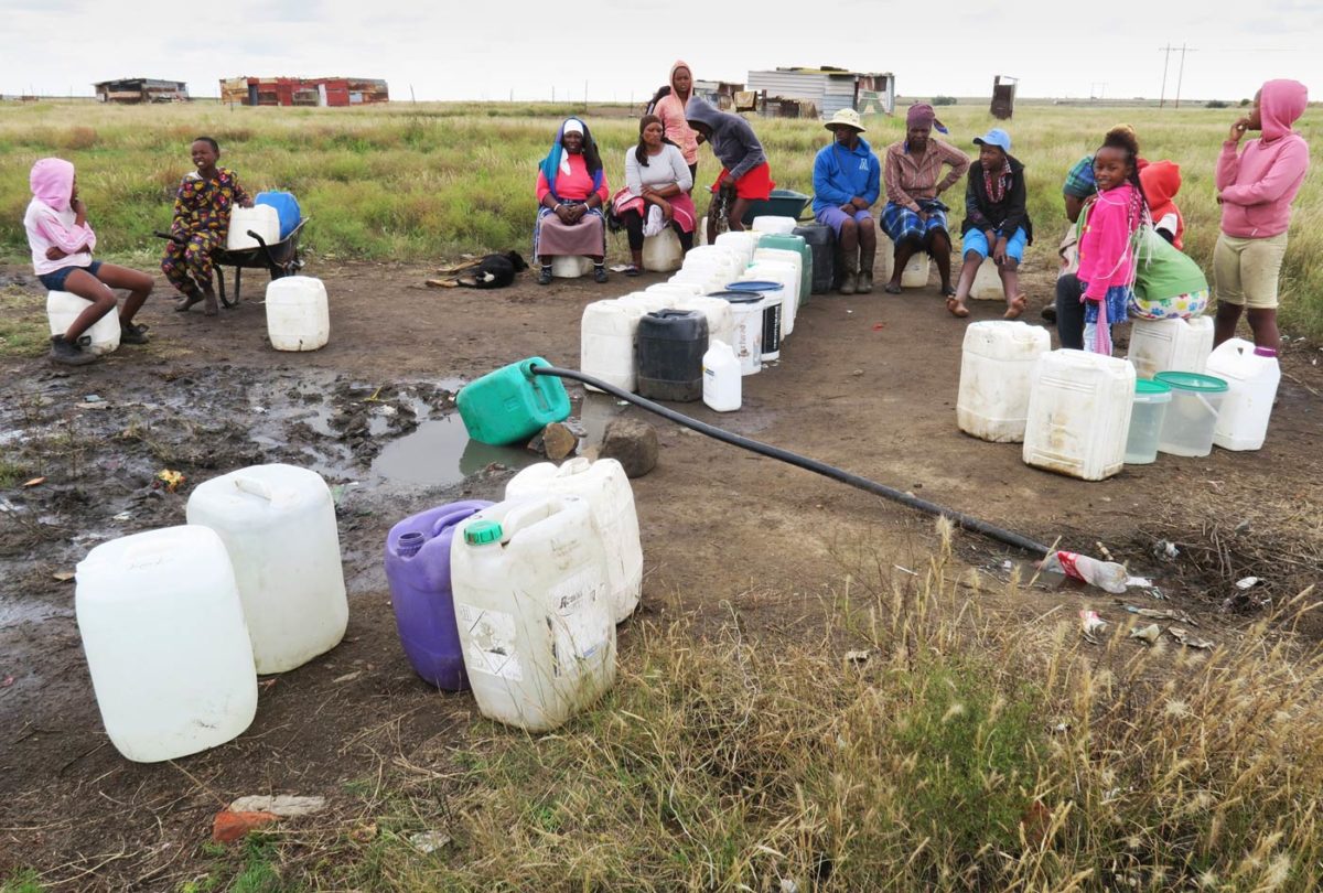 Residents of a new informal settlement outside Winburg gather to fill containers with water from a pipe supplied by the municipality