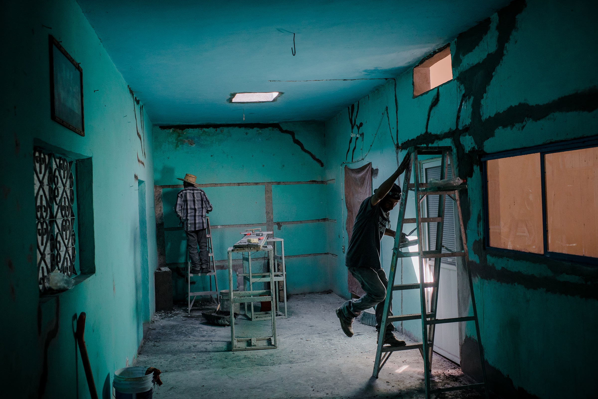 Two men doing construction repairs inside a room with blue walls