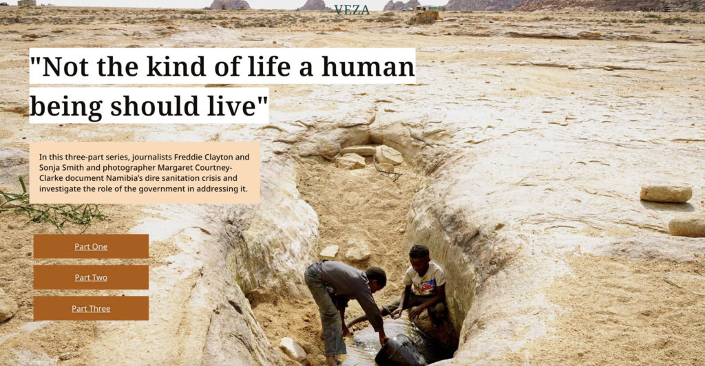 Photograph of two young boys in a deep dirt hole filling a bucket with water